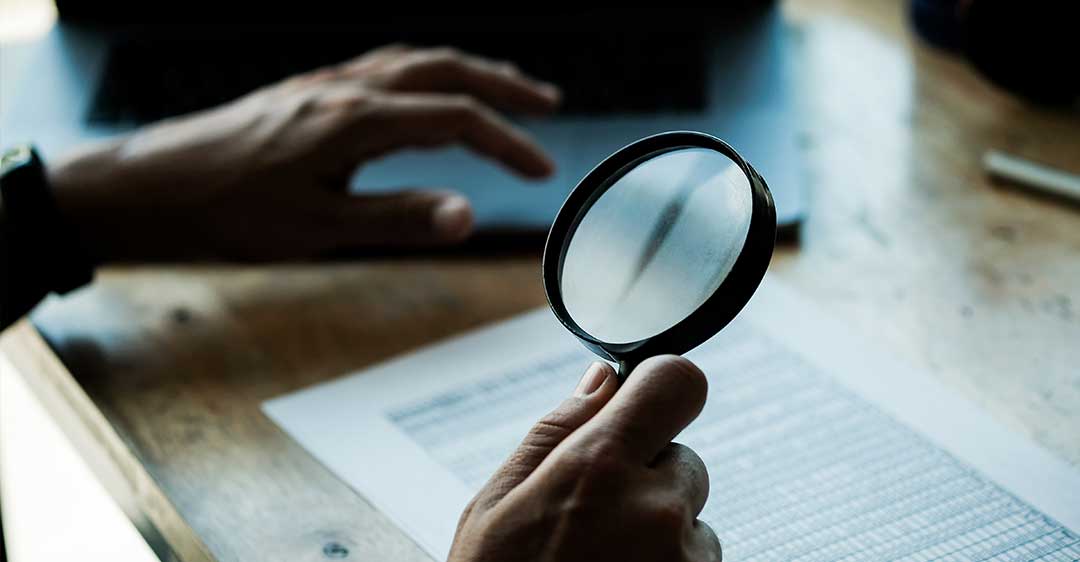 business man looking through magnifying glass at documents, breach of fiduciary duty