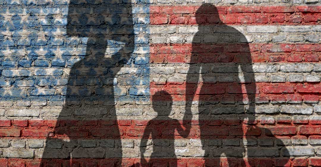 silhouette of family carrying luggage with US flag painted on brick wall, family petition