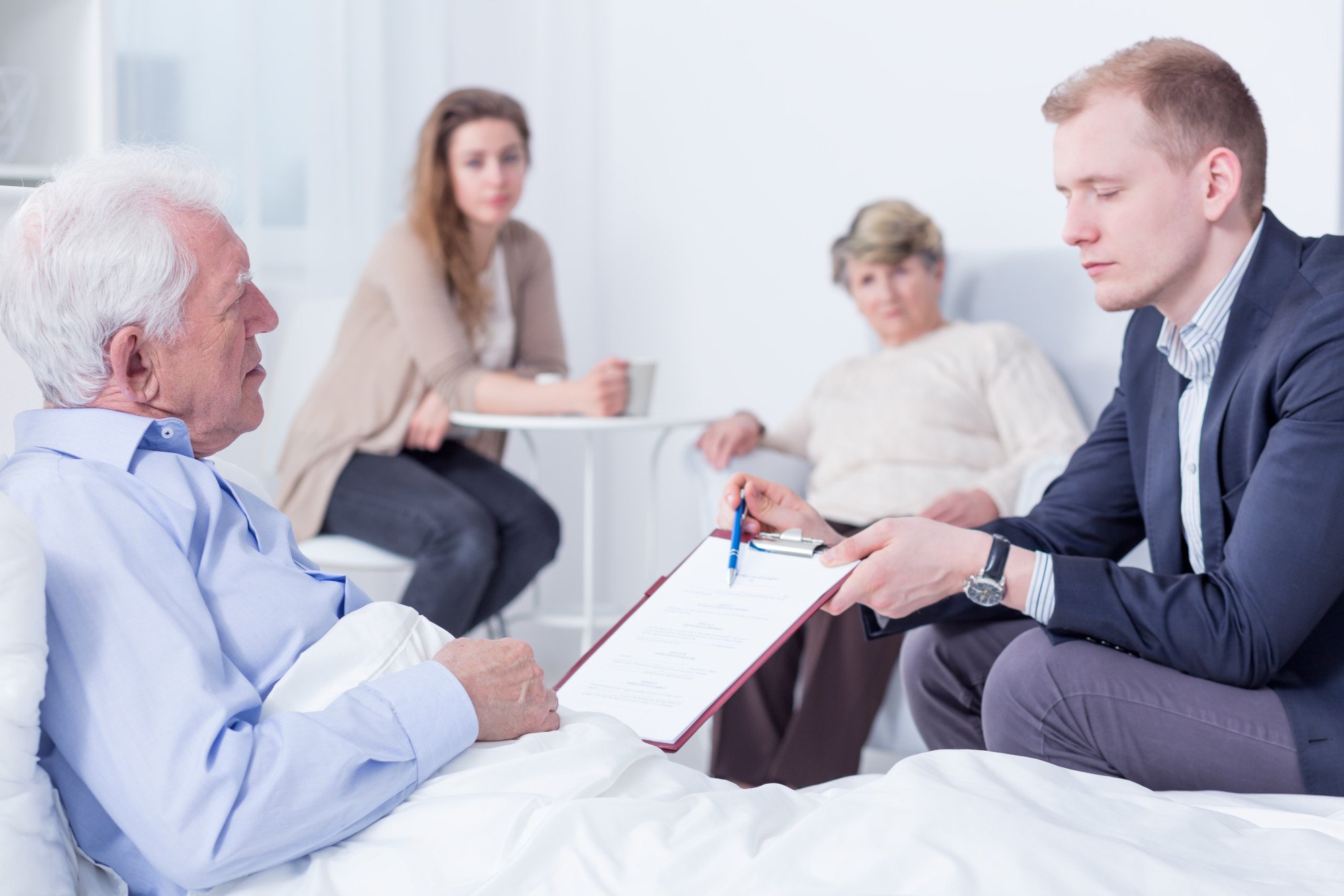 man reviewing documents with older man in bed, family members nearby, inheritance dispute