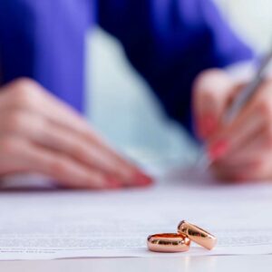 wedding rings in foreground, woman signing document in background, domestic contracts