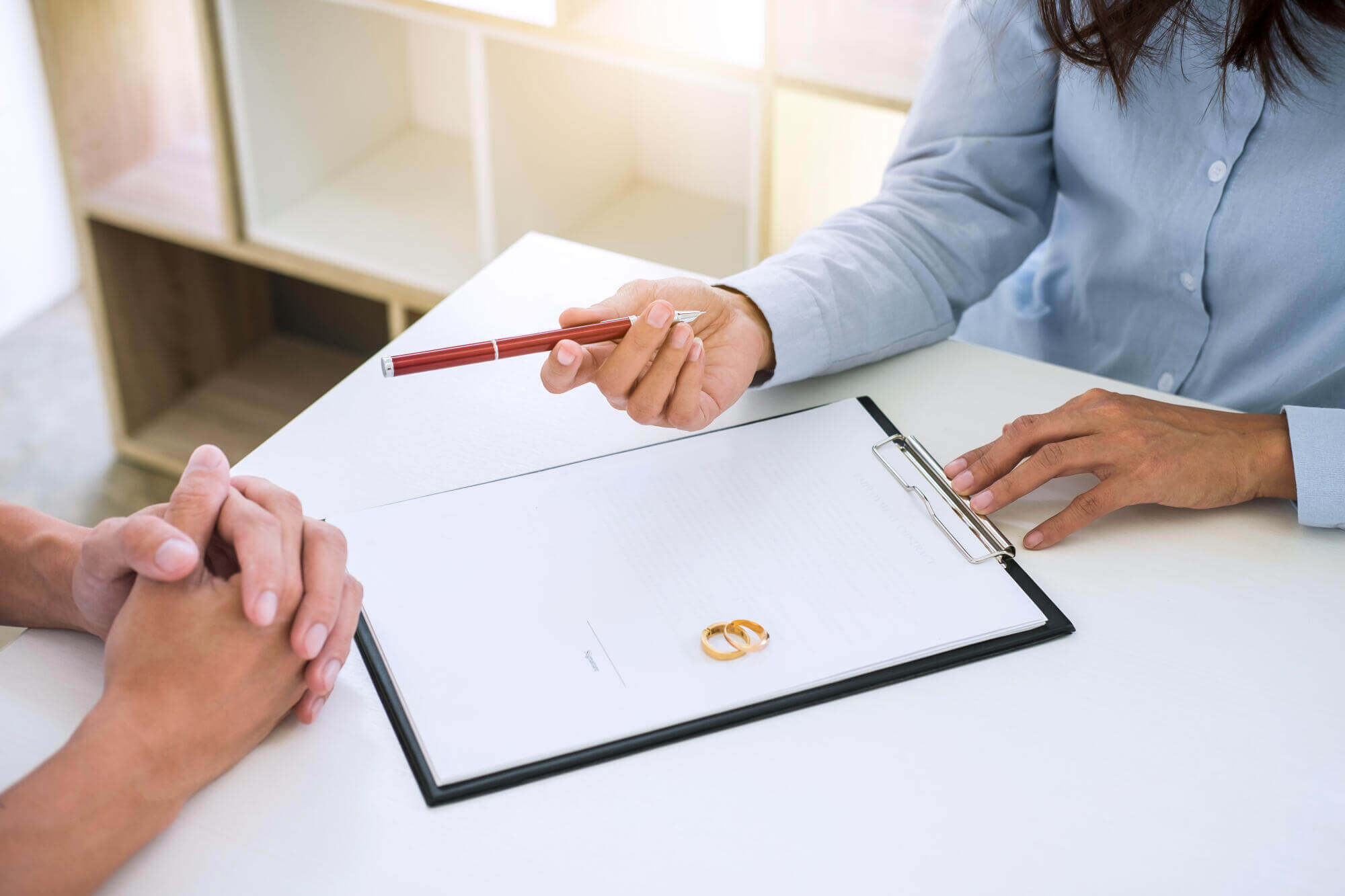 Lawyer discussing divorce paperwork with client, gold wedding rings on document