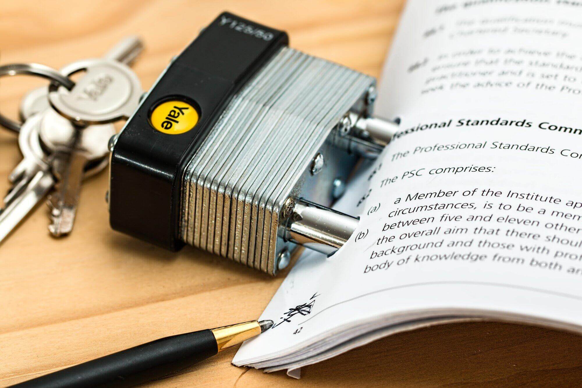 A padlock and a set of keys rest on top of an open document, with the lock's shackle threaded through the pages, symbolizing document security or restricted access, often essential for safeguarding Non-Compete Agreements.