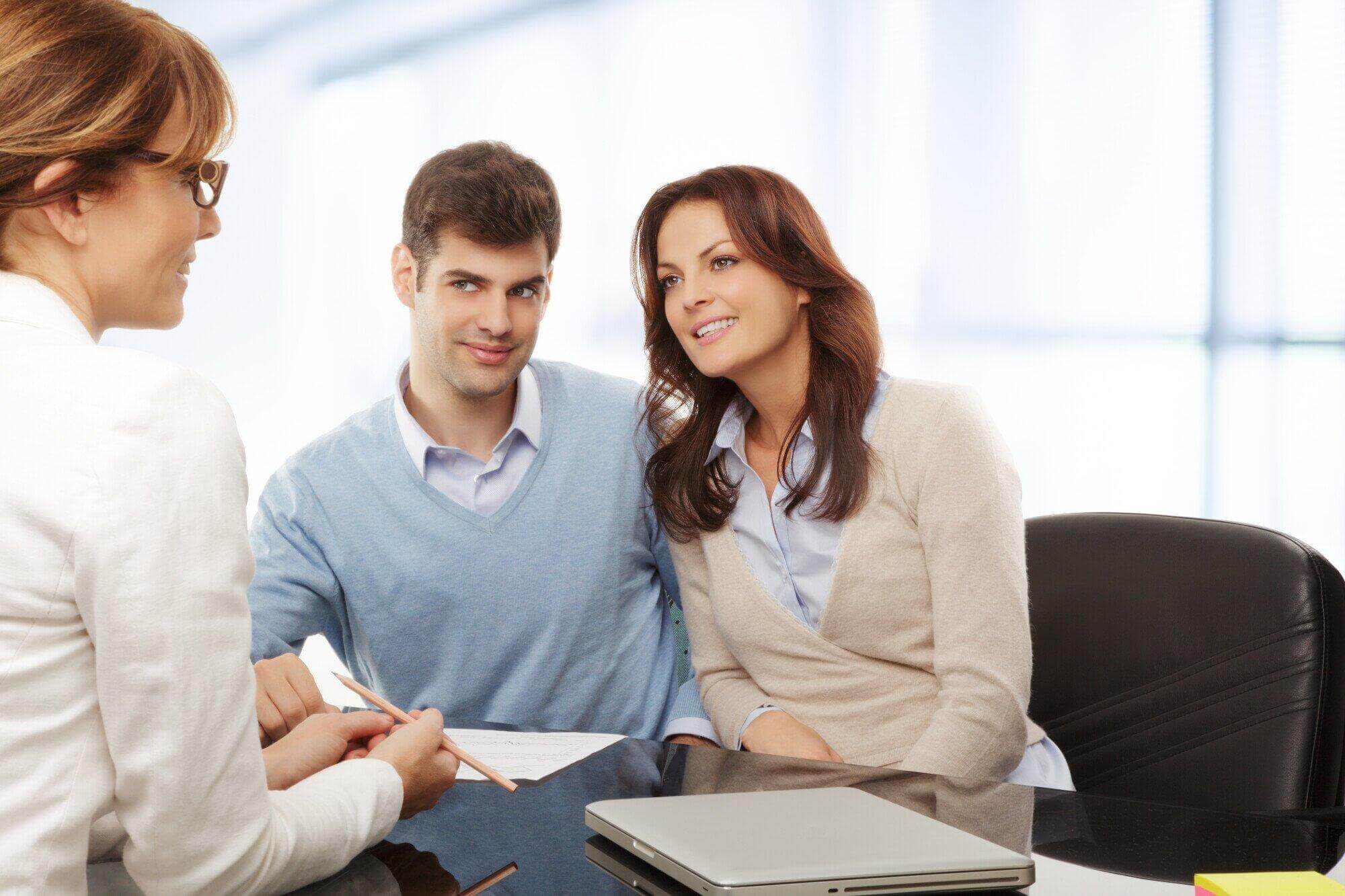 A professional florida attorney speaks with a smiling couple at a desk. The couple sits close together, looking attentive, with documents and a closed laptop in front of them—ideal for civil litigation attorney florida consultations.