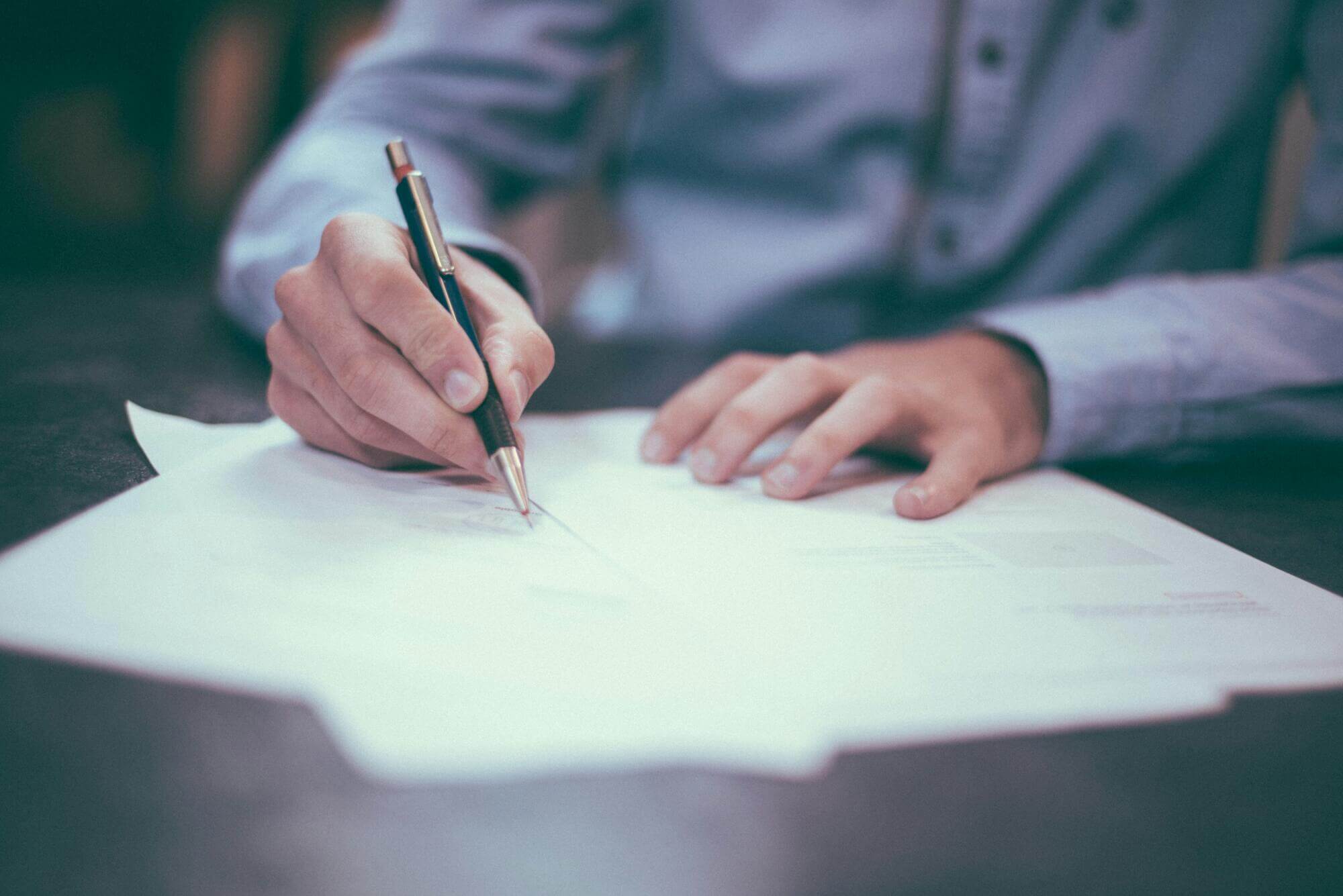 A florida attorney in a blue shirt sits at a table, holding a pen and writing on several sheets of white paper. The focus is on their hands and legal documents, reflecting the careful work of Dispute Resolution Attorneys.