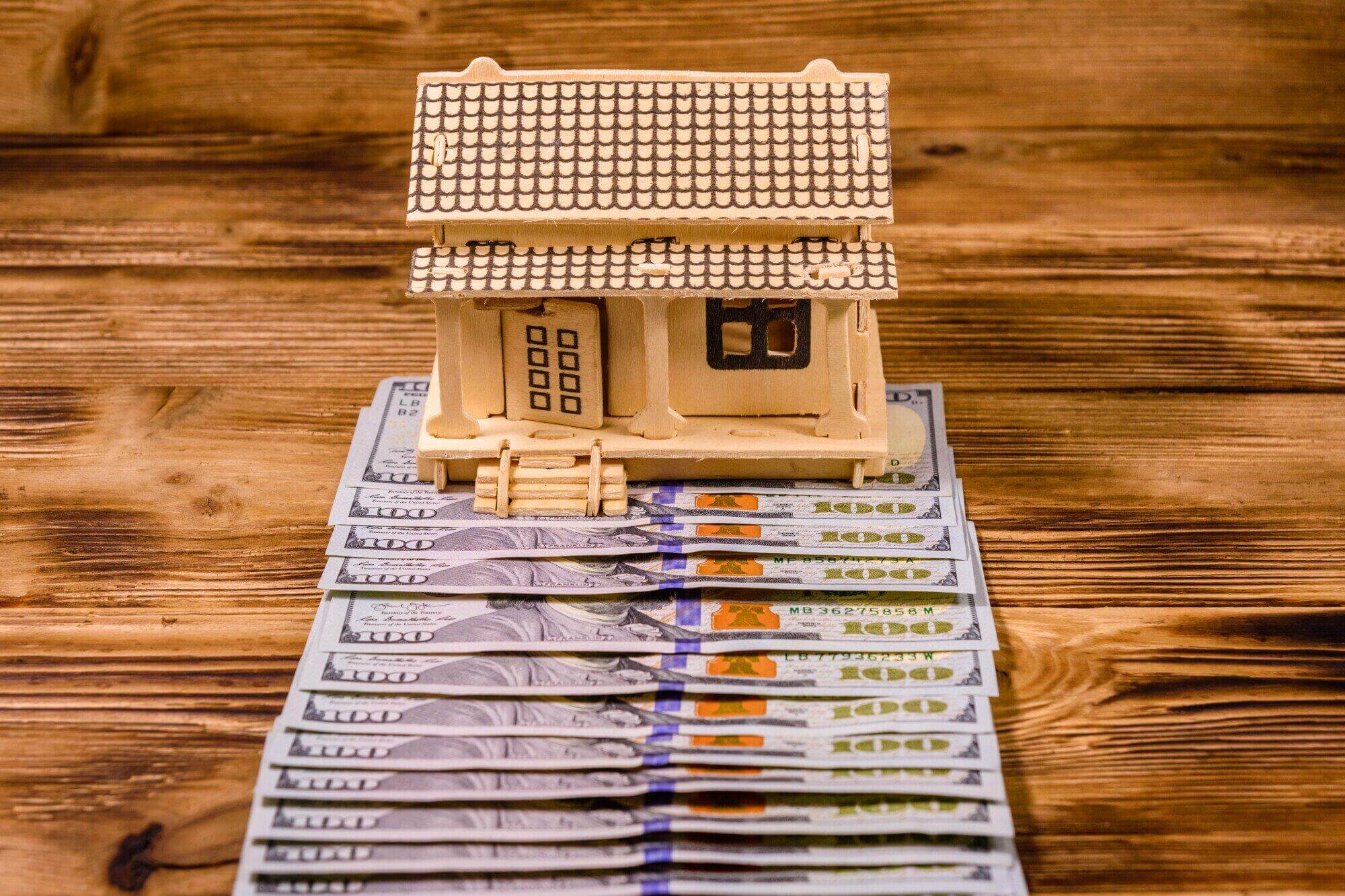 A small model house sits on $100 bills atop a wooden surface, suggesting real estate investment or home financing—a scene where a civil litigation attorney in Florida might assist with property disputes.