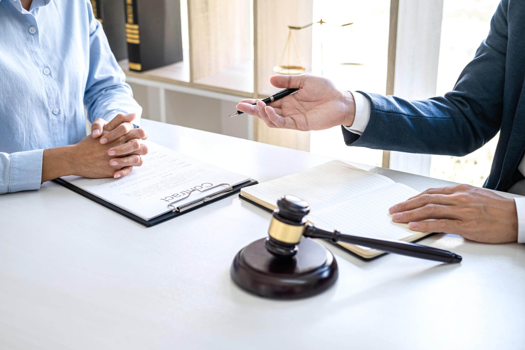 Two people sit at a desk with a gavel, legal contract, and notebook; one gestures with a pen while the other listens intently, portraying a florida attorney providing a legal consultation or dispute resolution discussion.