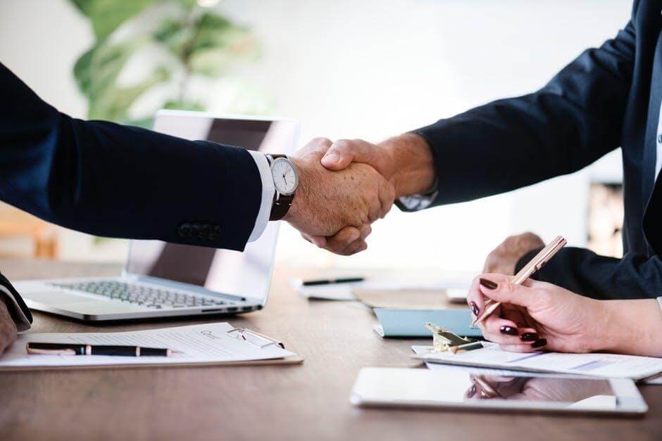 Two people in business attire shake hands across a desk with a laptop and documents, suggesting a successful meeting or agreement—an image reflecting the professionalism of Dispute Resolution Attorneys.