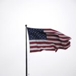 The American flag waves on a flagpole against a cloudy, overcast sky. The stars and stripes are clearly visible, reminiscent of the dedication shown by a civil litigation attorney in Florida—steadfast through any storm.