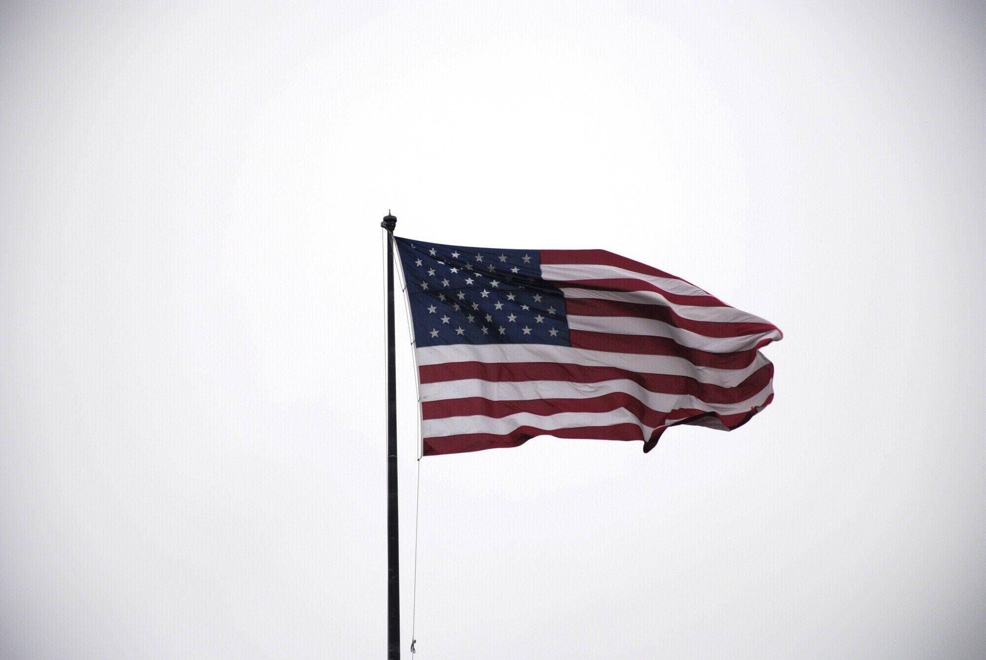 The American flag waves on a flagpole against a cloudy, overcast sky. The stars and stripes are clearly visible, reminiscent of the dedication shown by a civil litigation attorney in Florida—steadfast through any storm.
