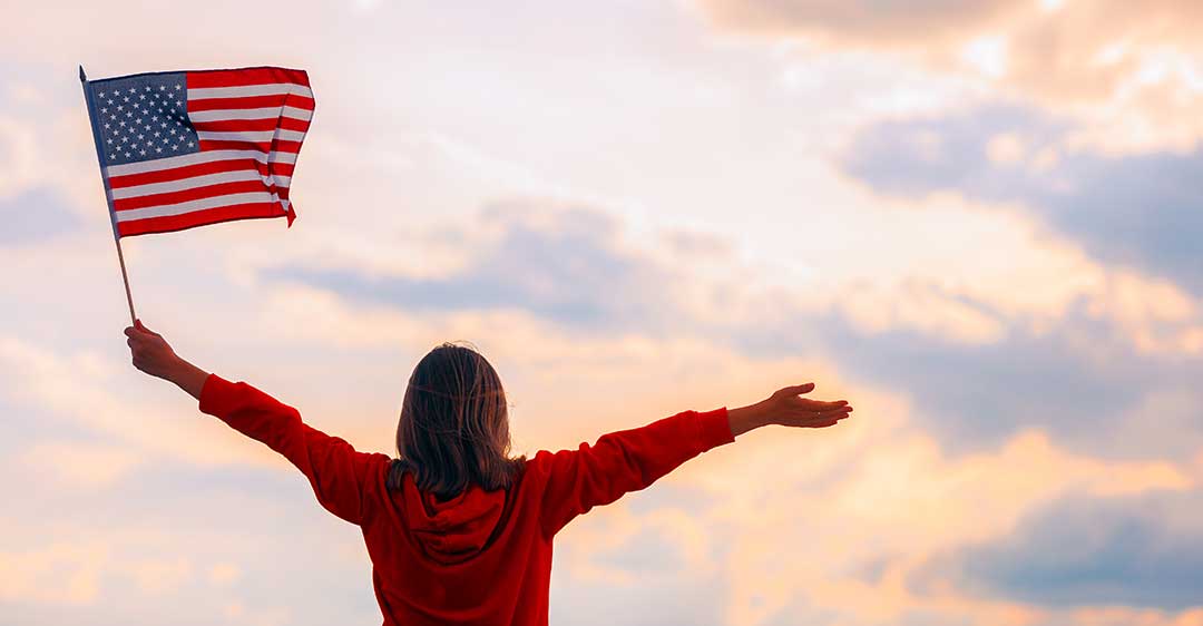 woman holding american flag looking at the sky with arms open, citizenship lawyer
